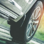 Llantas de un coche en una carretera mojada con agua salpicando, destacando el rendimiento de los neumáticos en condiciones de lluvia.